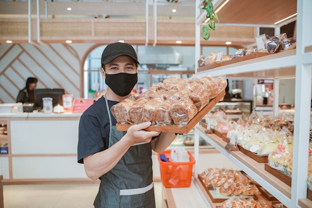 Beau travailleur asiatique à la boulangerie portant un masque au cours de la nouvelle normale ouverte aux entreprises