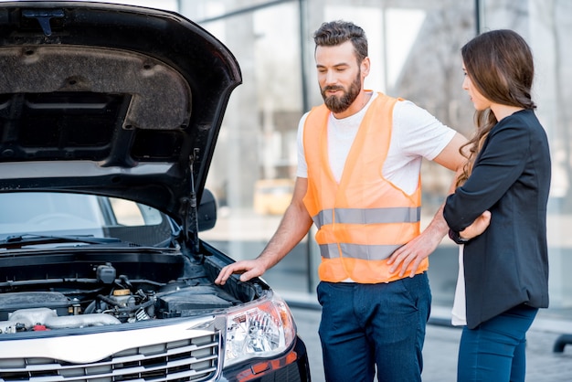 Beau travailleur de service consultant ou fournissant une assistance technique de la voiture cassée à la femme d'affaires se tenant près du bâtiment du centre de service