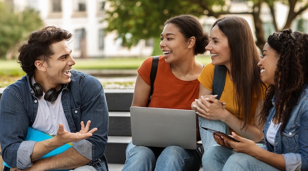 Un beau type de l'université qui parle à un groupe d'étudiantes heureuses à l'extérieur.