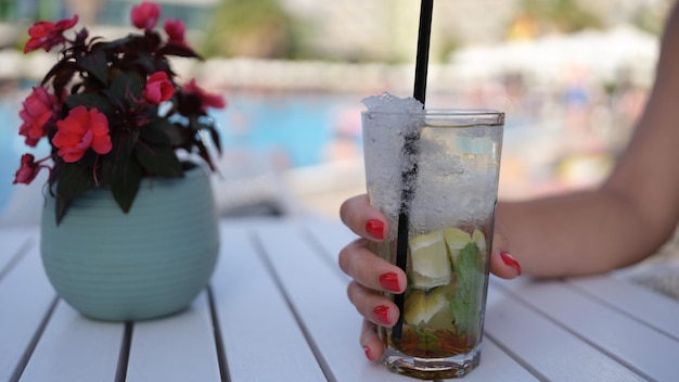 Beau verre avec cocktail rafraîchissant dans la main de la femme sur fond de piscine