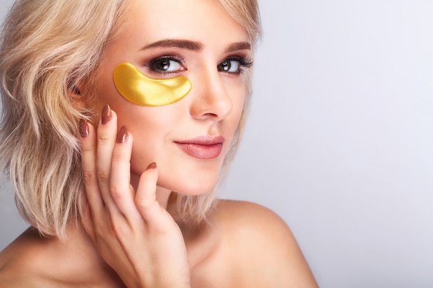 Beau visage de femme avec des correctifs d'or à l'hydrogel, masque de levage au collagène anti-rides sur une peau du visage saine et fraîche.