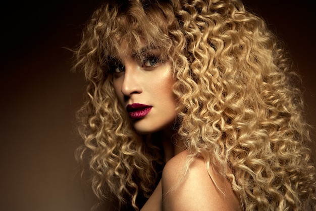 Beau visage d'un mannequin aux yeux bleus. Cheveux bouclés. Lèvres rouges.