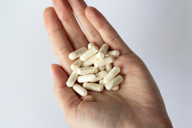 Beaucoup de capsules blanches dans la main d'une femme Compléments alimentaires et médicaments