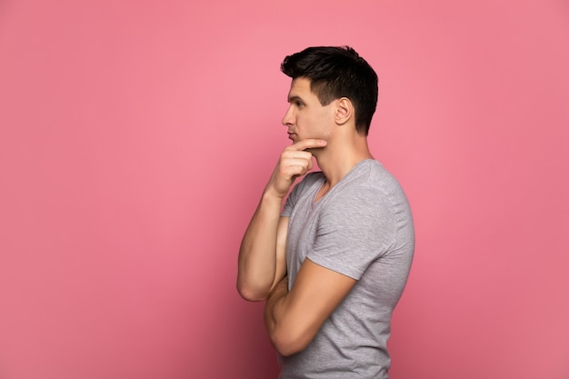 Beaucoup de choses à penser. un homme séduisant dans un t-shirt gris, qui se tient de profil et pense à quelque chose, tout en touchant son menton avec la main droite.