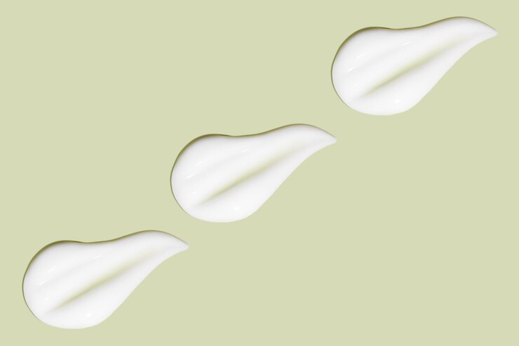 Photo beaucoup de frottis de crème cosmétique surface lisse et légère dans une rangée sous un angle vue de dessus texture de crème qui coule traits crémeux liquides sur fond vert bannière de fond cosmétique