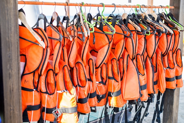 Beaucoup de gilets de sauvetage orange suspendus à des cintres.