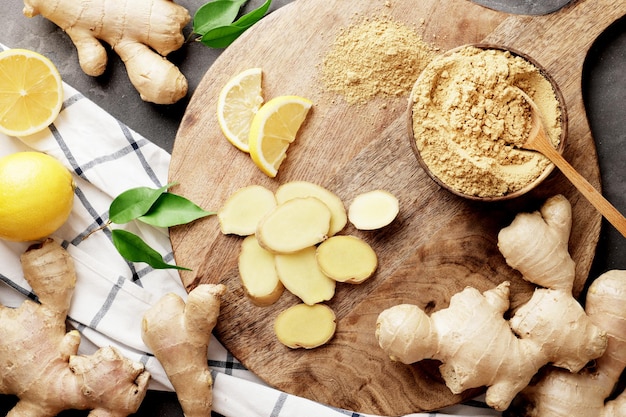 Beaucoup de gingembre différent sur une planche de cuisine en bois avec des citrons. Gingembre sec et frais, lames de gingembre et citrons. Un bol rempli d'épices au gingembre.