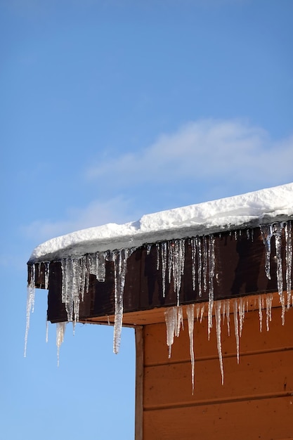 Beaucoup de glaces fondantes avec des gouttes de chute pendent en gros plan sur le bord du toit avec de la neige contre le bleu