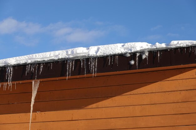 Photo beaucoup de glaces fondantes avec des gouttes de chute pendent en gros plan sur le toit plat avec de la neige contre le bleu