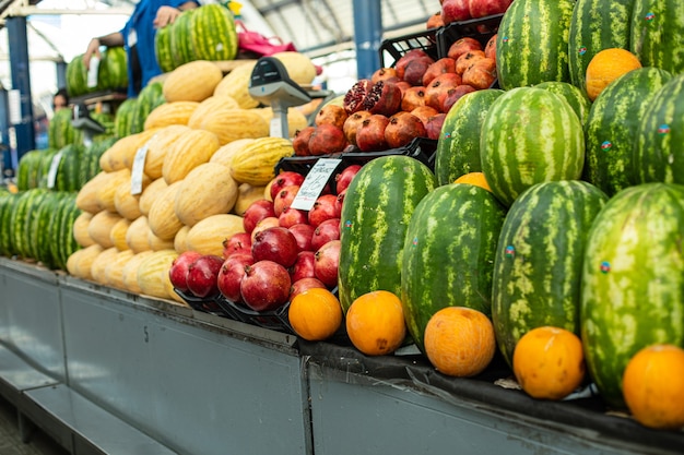 Beaucoup de grosses pastèques vertes debout à côté d'oranges et d'autres fruits sur l'étagère du supermarché.