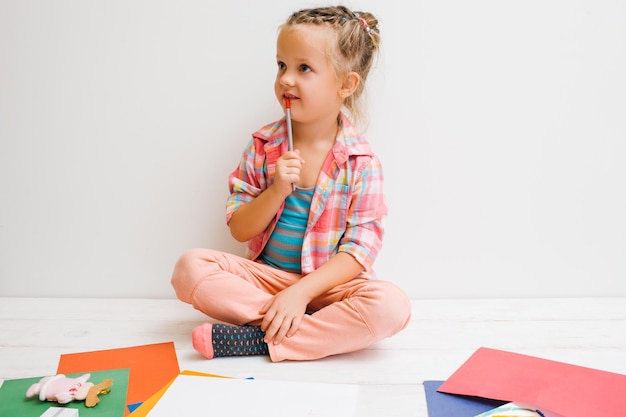 Beaucoup d'idées pour l'art Processus réfléchi Petite fille artiste sur fond blanc inventer une peinture intéressante Concept de pensée d'enfant rêvant