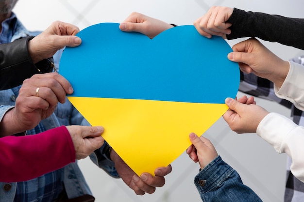 Photo beaucoup de mains de différentes personnes tenant un grand coeur aux couleurs du drapeau ukrainien liberté et soutien à l'ukraine arrêtez la guerre