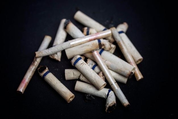 Beaucoup de mégots de cigarettes avec des traces de rouge à lèvres sur le filtre sur fond noir Tabagisme et mauvaise habitude en gros plan