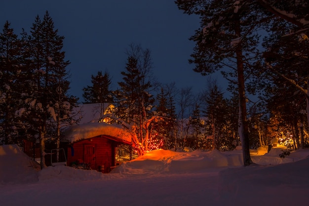 Beaucoup de neige dans les bois d'hiver du soir. Une maison avec des lumières et une guirlande sur l'arbre