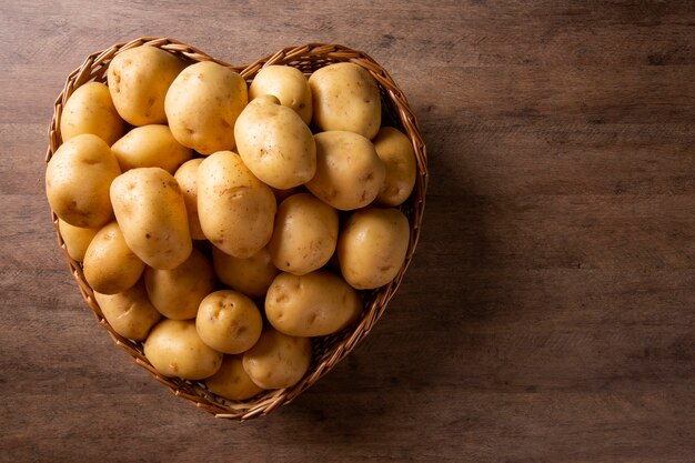 Photo beaucoup de pommes de terre dans le panier coeur sur une surface en bois.