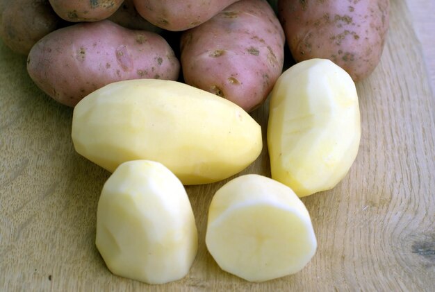 Photo beaucoup de pommes de terre pelées et non pelées sur le bureau de la cuisine dans le processus de cuisson des aliments vue rapprochée