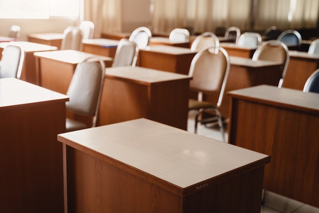 Beaucoup de tables et chaises en bois bien disposées dans la classe universitaire mais pas d'étudiant. Salle de classe vide sans élève en raison de la fermeture de l'école pendant la pandémie de COVID-19.