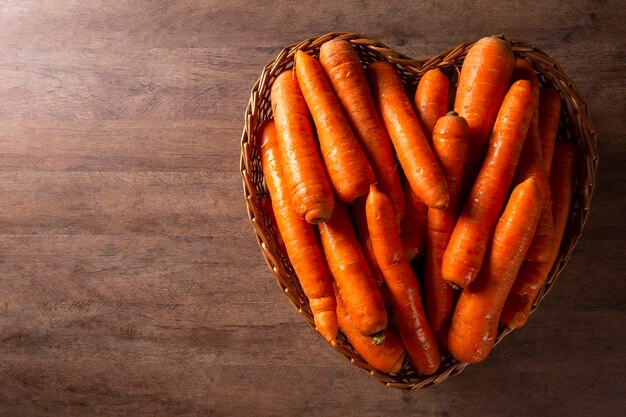 Beaucoup de tas de carottes dans le panier coeur sur fond de bois.