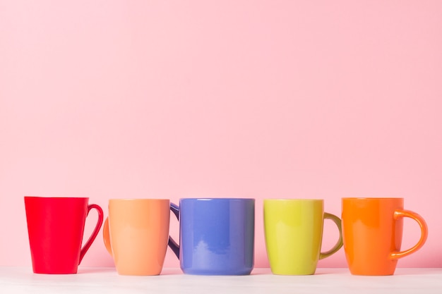 Beaucoup de tasses de café ou de thé multicolores sur fond rose. Le concept d'une entreprise conviviale, d'une grande famille, de rencontres entre amis pour une tasse de thé ou de café.