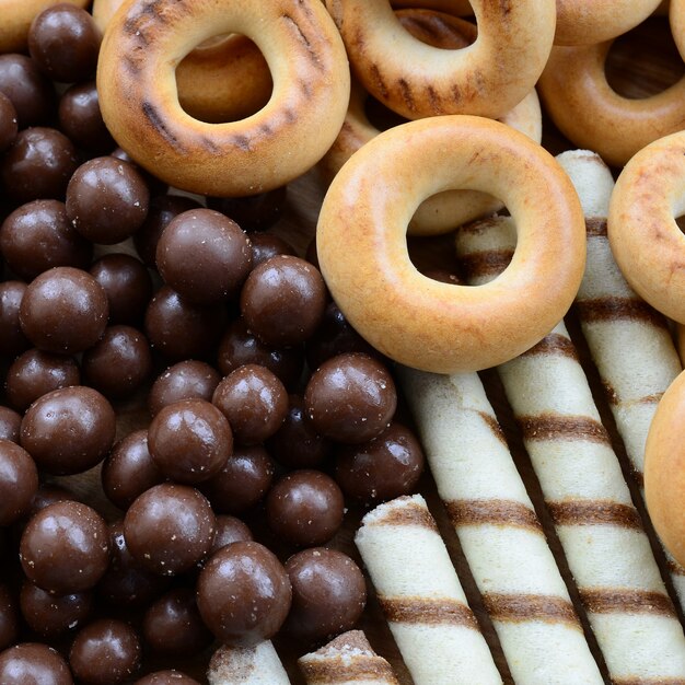 Beaucoup de tubules sucrés croustillants, de boules de chocolat fondant et de bagels jaunes reposent sur une surface en bois. Vue rapprochée