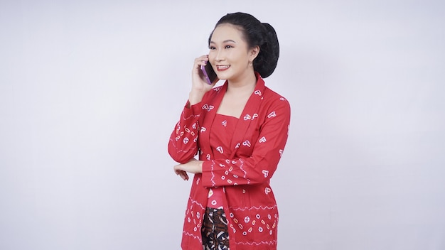 Beauté asiatique en kebaya au téléphone via smartphone isolé sur fond blanc