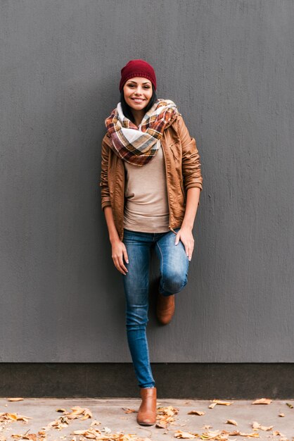 Beauté d'automne. Belle jeune femme se penchant sur le mur gris et souriant avec des feuilles tombées