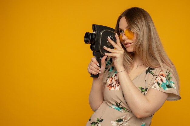 Beauté avec caméra. Joyeuse jeune femme tenant une caméra et posant sur fond jaune