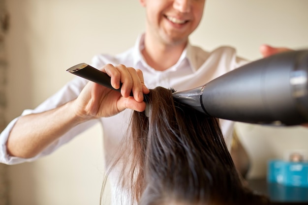 beauté, coiffure, brushing et concept de personnes - gros plan d'un coiffeur avec ventilateur et brosse faisant un style chaud au salon de coiffure