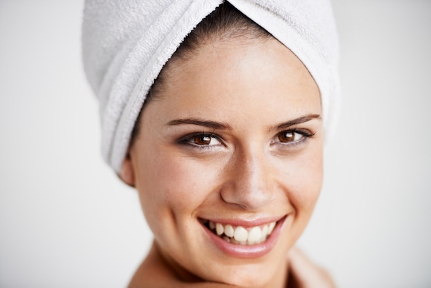 Photo la beauté du sourire et la femme avec une serviette dans un studio pour le bien-être de la santé et la routine naturelle du visage soin de la peau heureux et portrait de jeune mannequin avec traitement de dermatologie faciale par fond gris