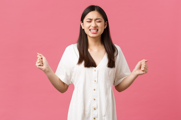 Beauté, émotions des gens et concept de loisirs d'été. Petite amie qui pleure désespérée et frustrée est trompée, serre les poings haineux et folle, grimaçant de chagrin douloureux, mur rose