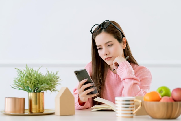 Beauté femme asiatique brune cheveux longs main tenir smartphone travail à la maison avec bonheur et joyeux fond de salle blanche