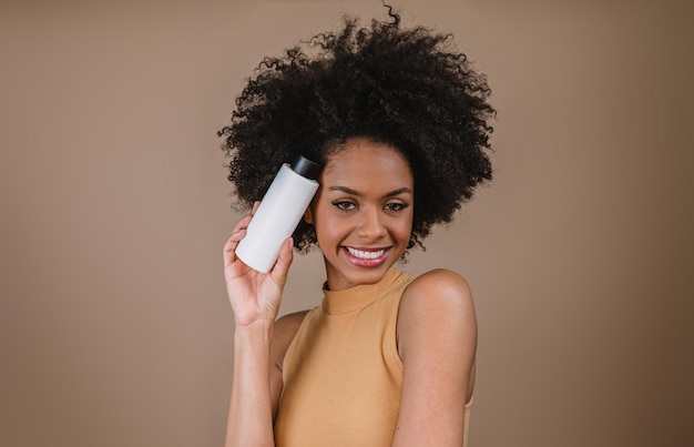 Beauté femme latine avec une coiffure afro femme brésilienne tenant un emballage de shampoing vierge