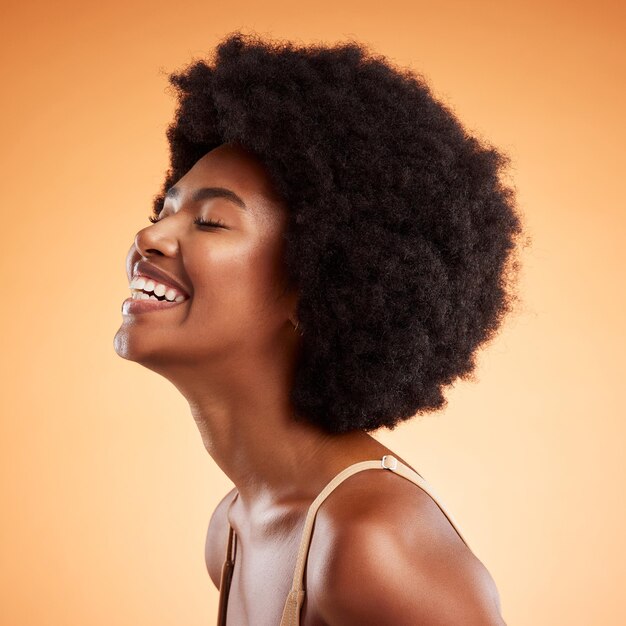 Beauté femme noire et rire bien-être soins de la peau et maquillage naturel esthétique peau éclatante et cosmétiques propres sur fond de studio orange Sourire heureux et jeune modèle visage cheveux afro et drôle