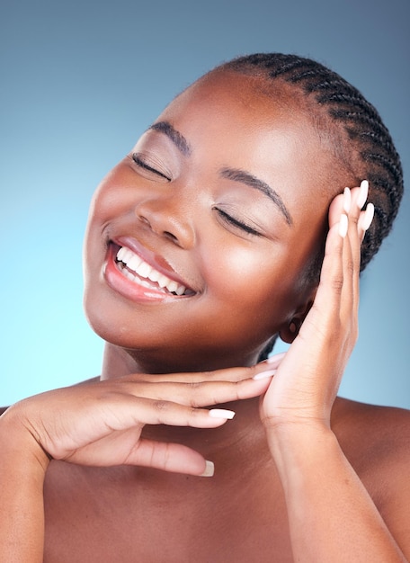 Beauté femme noire et sourire avec des cosmétiques de soin de la peau et du bien-être du visage dans un studio Maquillage et dermatologie sur fond bleu avec éclat et brillance de la peau grâce au traitement avec manucure et détox calme