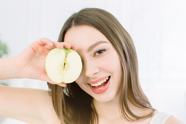 Beauté femme souriante tenant la moitié de la pomme verte. La jeune fille ferme un œil avec une demi-pomme.