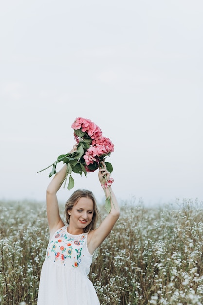 Beauté fille blonde aux yeux bleus et cheveux longs, détient un bouquet de fleurs roses et de sourires