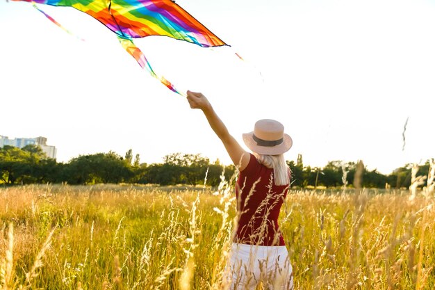 Beauté fille courir avec cerf-volant sur le terrain. Belle jeune femme avec un cerf-volant coloré volant sur un ciel bleu clair. Libre, concept de liberté. Émotions, mode de vie sain