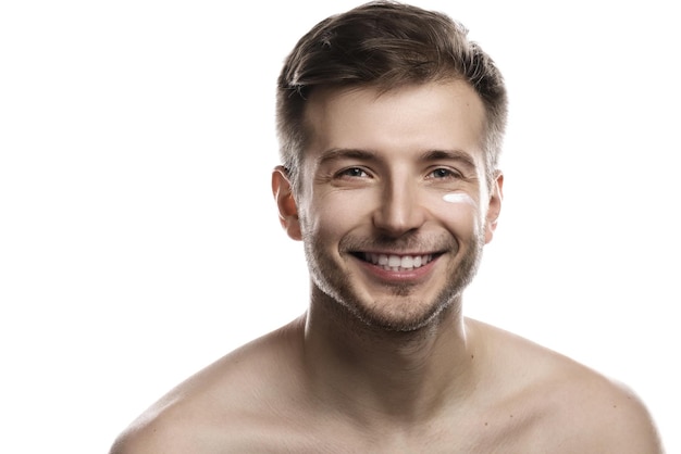 La beauté des hommes. Le jeune homme applique une crème hydratante et anti-vieillissante sur son visage sur fond blanc