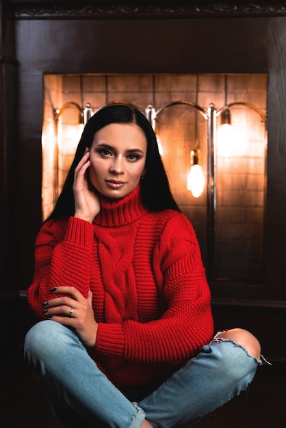 Beauté jeune femme brune assise près de la cheminée à la maison