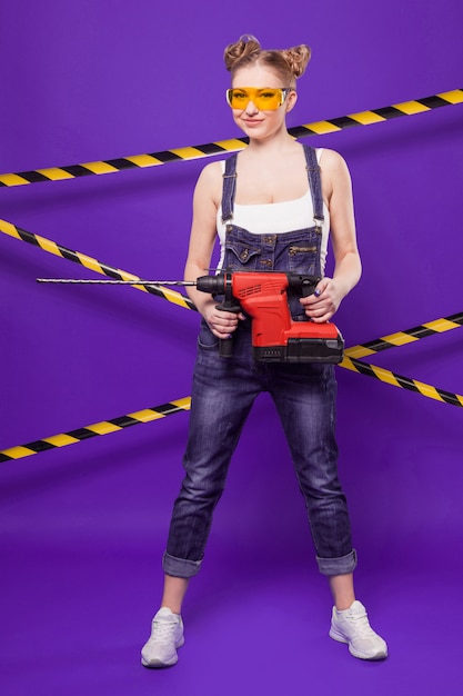 Beauté Jeune Fille De Constructeur En Combinaison De Denim Et Lunettes Se Tenir Avec Grosse Perceuse