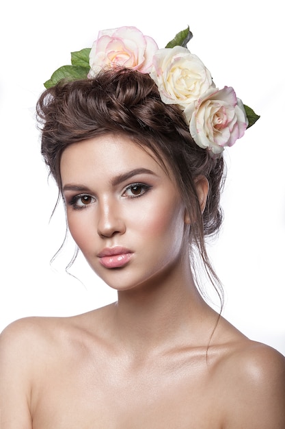 Beauté jeune fille, peau propre, beau maquillage, tresses de coiffure et fleurs roses dans les cheveux. Tonalité claire sur fond blanc.