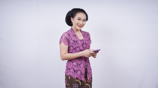 Beauté en kebaya jouant avec un téléphone portable isolé sur fond blanc