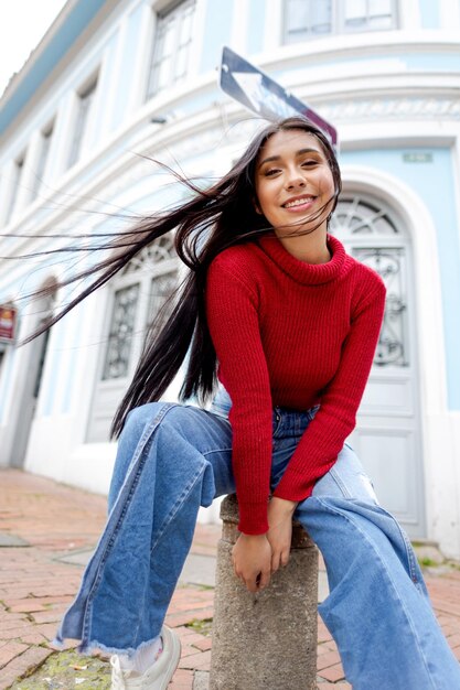 Beauté latina dans un cadre historique Portrait d'une femme souriante aux cheveux noirs et à la veste rouge contre une maison bleue vintage