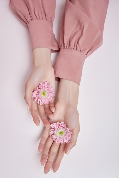 Beauté mains femme avec des fleurs roses dans ses mains sur la table. Cosmétique naturel pour le soin de la peau des mains