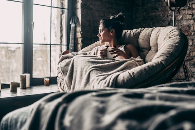 beauté à la maison. Jolie jeune femme recouverte d'une couverture regardant par la fenêtre