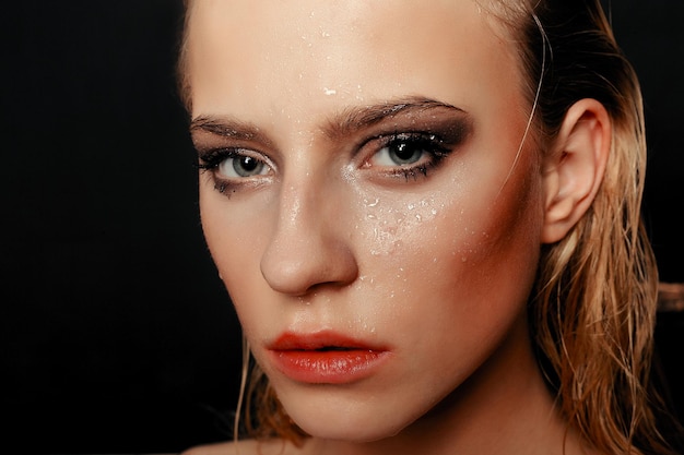 Beauté mannequin fille maquillage naturel cheveux mouillés sur fond d'or noir dans des tons chauds. Portrait de jeune femme avec le maquillage de mode