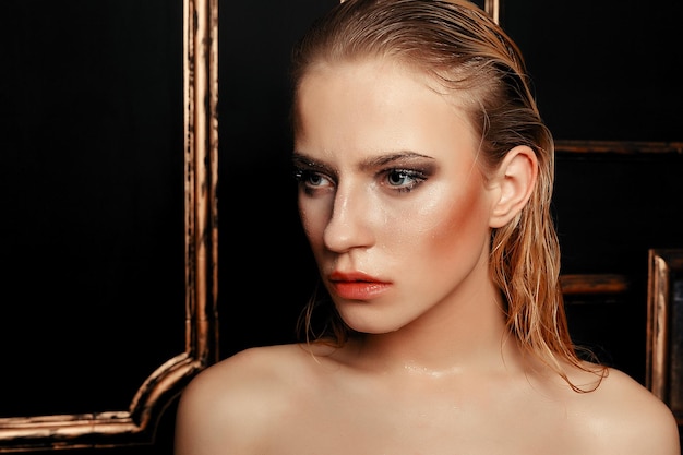 Beauté mannequin fille maquillage naturel cheveux mouillés sur fond d'or noir dans des tons chauds. Portrait de jeune femme avec le maquillage de mode