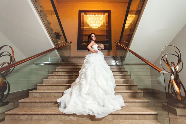 Beauté mariée adulte en robe de mariée blanche debout à l'intérieur dans les escaliers