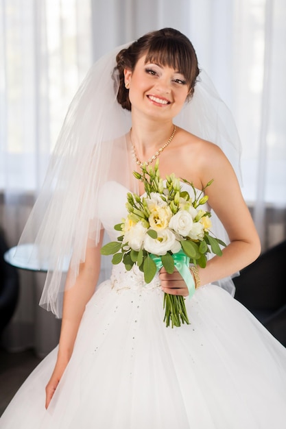 Beauté mariée souriante avec bouquet dans la chambre