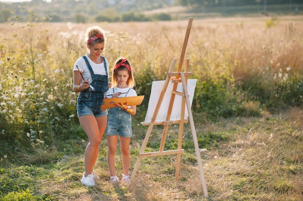 Beauté mère peindre avec sa petite fille. Femme élégante, dessiner l'image avec une petite fille. Enfant mignon dans un t-shirt blanc et un jean bleu.
